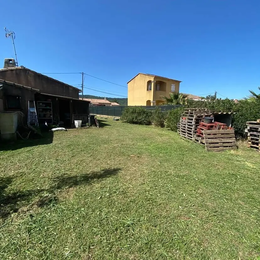 Grande pelouse tondue devant un abri de jardin et une maison ocre, La Motte